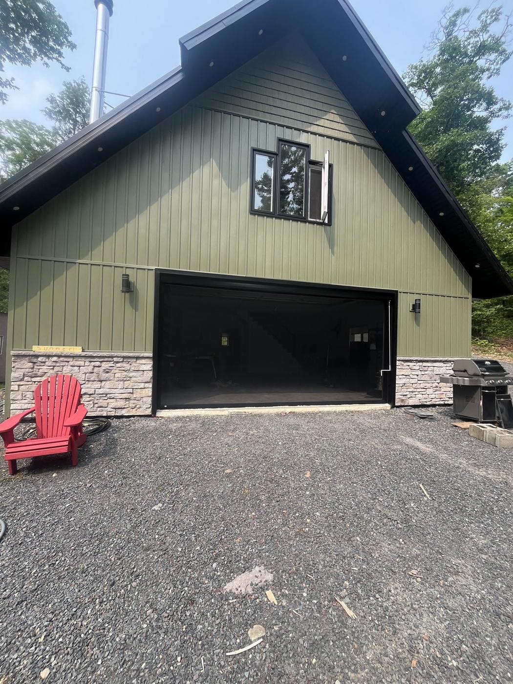 Olive green building with a stone base and a wide open garage opening