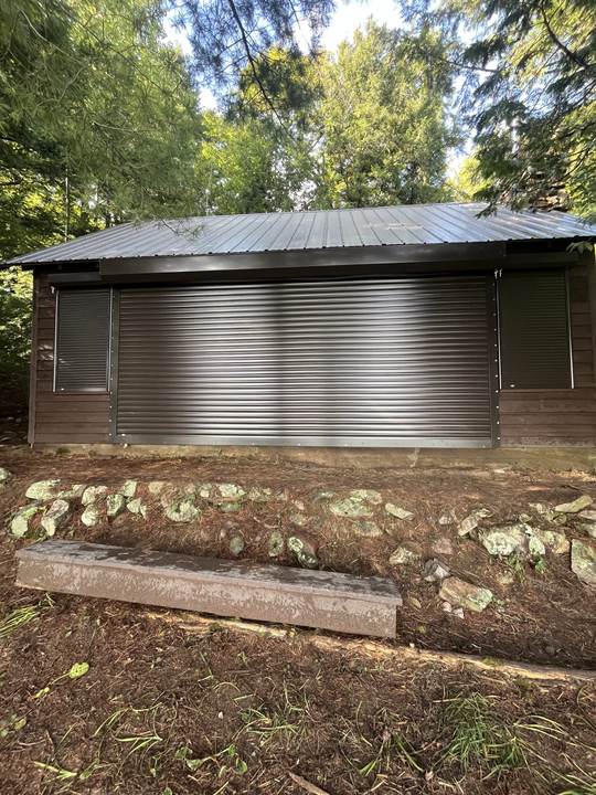 Brown building in the woods with a silver roll shutter and side windows
