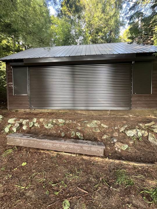 Brown building with a metal roof and a wide silver roll shutter