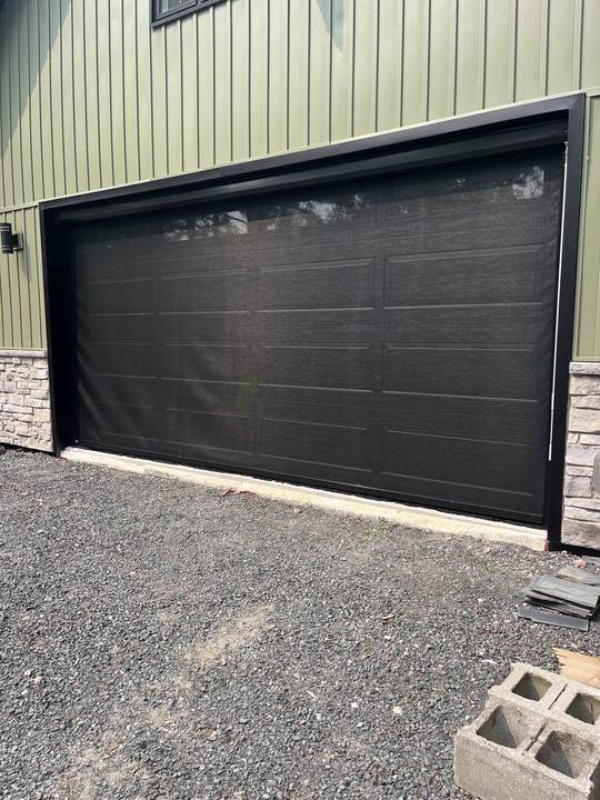 Closed dark garage door on an olive green building with a stone base