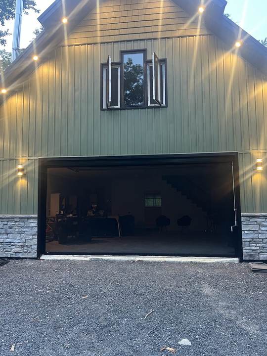 Olive green building at dusk with exterior lights and an open garage opening