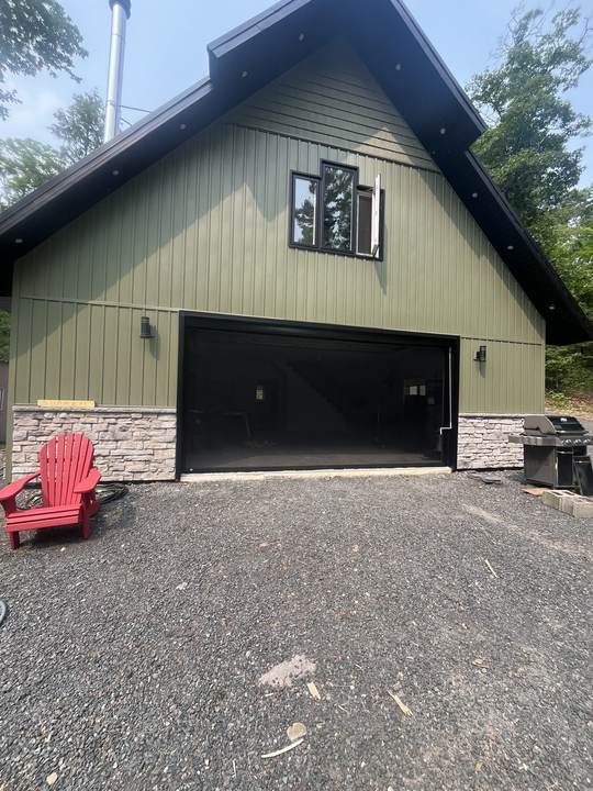 Olive green building with a stone base and a wide open garage opening