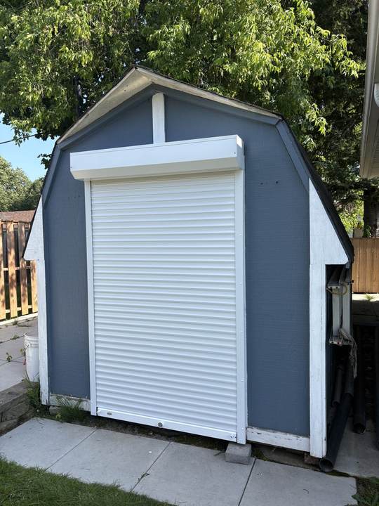 Grey shed with white trim and a white roll shutter door