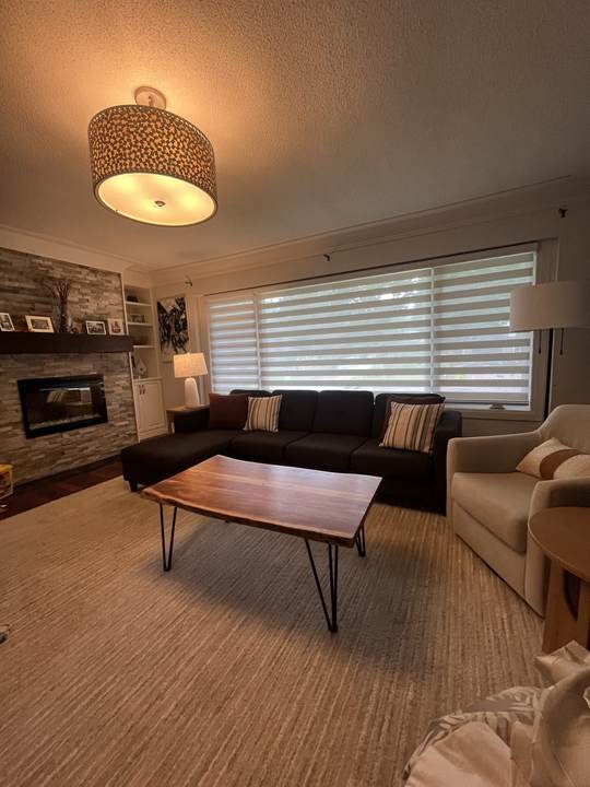 Living room seating with a wood coffee table, a stone fireplace and window blinds