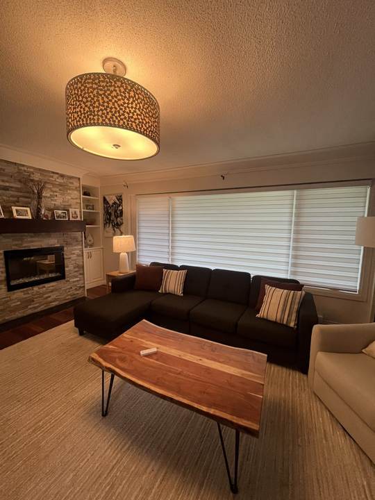 Living room with a dark sectional, a wood coffee table, a stacked stone fireplace and white horizontal blinds